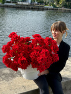 A person holding a large bouquet of red roses in front of a body of water.