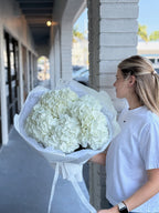 A person holding a large bouquet of white hydrangea flowers.