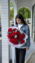 Person holding a bouquet of red roses outside a building.