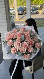 A person holding a large bouquet of pink Mondial roses and fragrant eucalyptus.