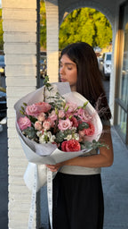 A person holding a bouquet of flowers with a variety of colors, predominantly pink and green, wrapped in paper.