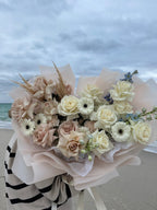 A floral bouquet featuring a variety of flowers in pastel hues, arranged in a cascade, with a striped beige and white fabric serving as a backdrop.