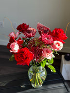 A bouquet of red and pink flowers including roses and other assorted flowers, placed in a clear glass vase.