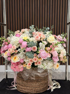 A large, wicker basket containing an assortment of cut flowers including peonies and piano roses, arranged in a bouquet.