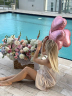 A person sitting beside a large flower box with a variety of flowers in shades of pink, white, and green, and a balloon in the shape of a heart.