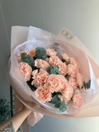 A bouquet of pink carnations wrapped in paper with a visible brand name on the tape.