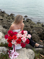 A person sitting on a rock by the water with a large bouquet of red and pink roses.