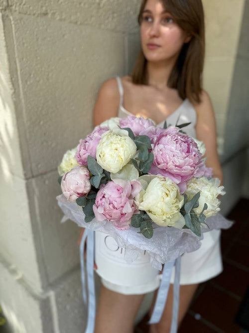 A person holding a luxurious box of white and pink peonies.