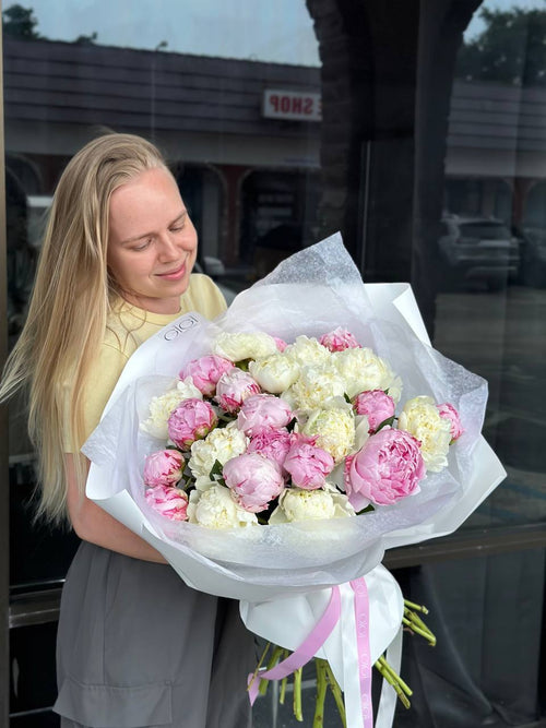 A person holding a large bouquet of white and pink peonies.